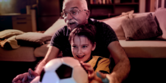 young male child sits on the lap of his grandfather while they watch television